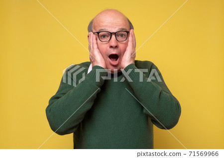 Surprised caucasian man with glasses holding hands near face. 71569966