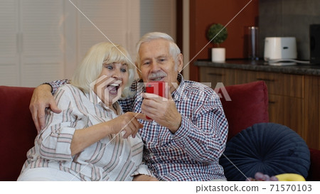 Grandmother and grandfather making video call online on mobile phone at home. Smiling elderly couple Grandmother and grandfather making video call online on mobile phone at home. Smiling elderly couple 71570103