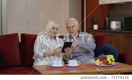 Senior old couple grandparents talking and using digital tablet computer at home. Internet shopping Senior old couple grandparents talking and using digital tablet computer at home. Internet shopping 71570116