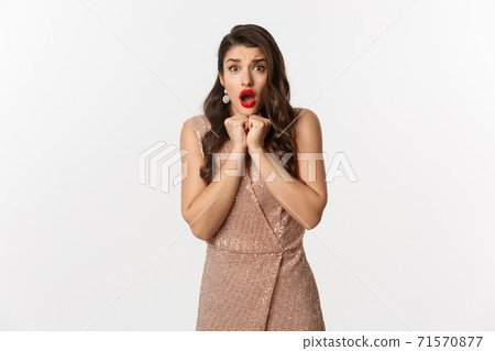 Image of beautiful woman celebrating New Year, looking scared and worried at camera, gasping amazed, wearing evening dress, standing over white background 71570877