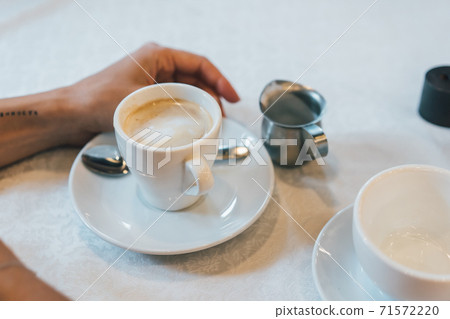 Small white cup of cappuccino stands on the table 71572220