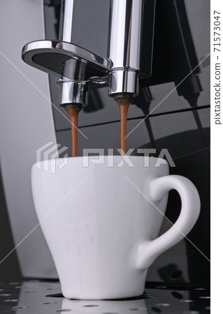 Wake-up coffee espresso with roasted Arabica coffee beans flows under pressure into white Cup. Preparation morning aromatic espresso coffee beans from professional coffee machine. Vertical video 71573047