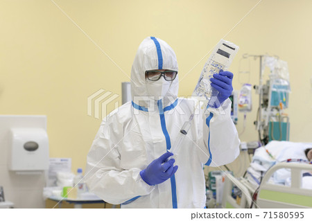 Male nurse with protective coverall clothing in intensive care unit. Nurse is drawing up into thy syringe saline. The nurse caring for a patient with covid-19. Male nurse with protective coverall clothing in intensive care unit. Nurse is drawing up into thy syringe saline. The nurse caring for a patient with covid-19. 71580595