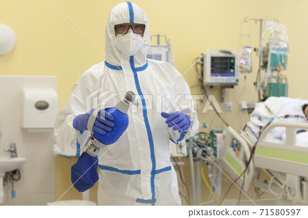 Male nurse with protective coverall clothing in intensive care unit. Nurse is holding breathing bag.. The nurse caring for a patient who fell ill with a new type of coronavirus covid-19. 71580597