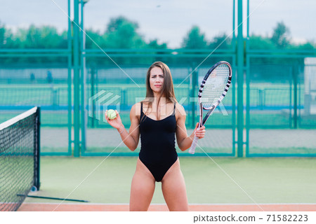 Beautiful young sport female dressed in bodysuit on tennis court 71582223