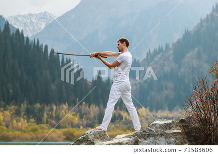 A young man stands on a large stone and holds a Japanese sword in his hands. A young man stands on a large stone and holds a Japanese sword in his hands. 71583606