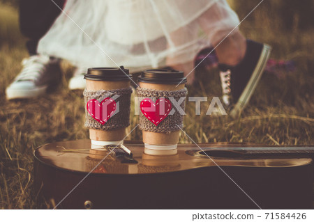 Romantic couple hugging while having picnic in sunset light. Coffee cup cozy knitted sleeve with felt red heart. 71584426