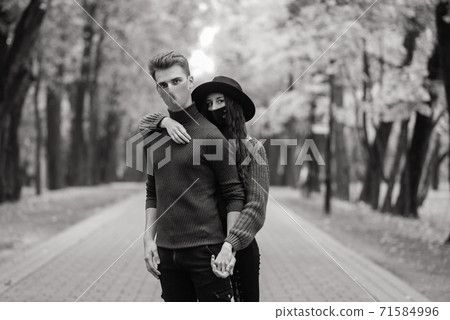 Young red haired woman puts on face mask while walking with young man in autumn park. Young red haired woman puts on face mask while walking with young man in autumn park. 71584996