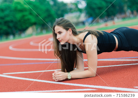 A female coach with dark hair stands on the red running track of the stadium A female coach with dark hair stands on the red running track of the stadium 71586239