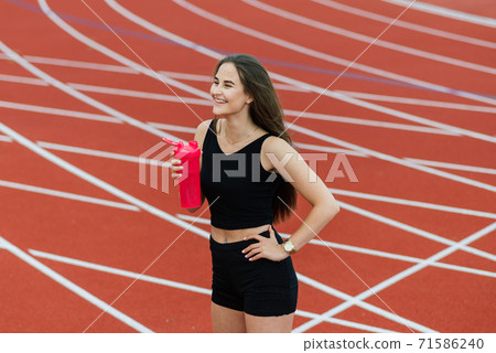 A female coach with dark hair stands on the red running track of the stadium A female coach with dark hair stands on the red running track of the stadium 71586240