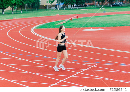 A female coach with dark hair stands on the red running track of the stadium A female coach with dark hair stands on the red running track of the stadium 71586241