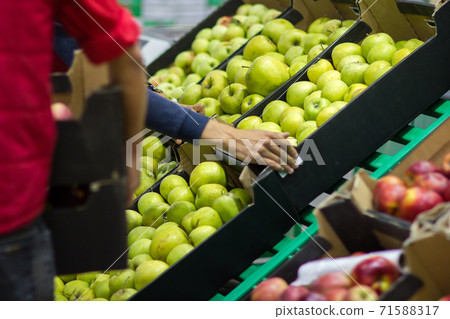 Young man seller lays out fresh fruits of the box on the grocery store 71588317