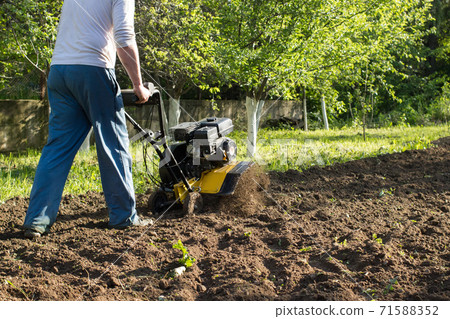 A perspective view of a man during soil plow process by motor cultivator A perspective view of a man during soil plow process by motor cultivator 71588352