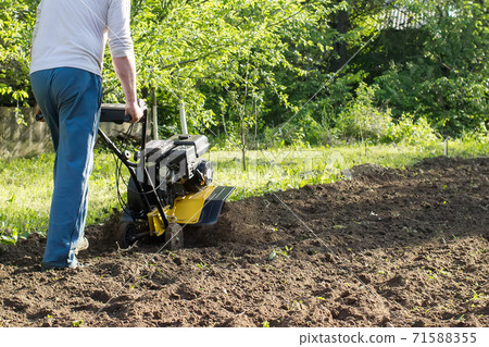 A man during soil plow process by motor cultivator perspective view A man during soil plow process by motor cultivator perspective view 71588355