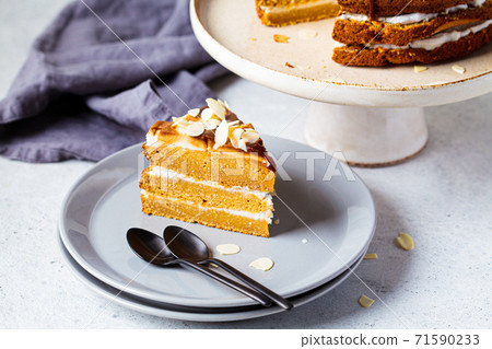 Piece of vegan cake on gray plate. Homemade carrot cake with white cream, caramel and nuts. 71590233