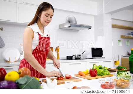 Female chef in red apron uses knife to cut tomato. Concept woman preparing meals at home. Female chef in red apron uses knife to cut tomato. Concept woman preparing meals at home. 71590644