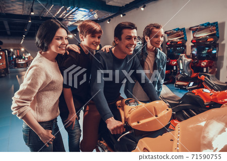 Dad sits on toy motorcycle while family is nearby Dad sits on toy motorcycle while family is nearby 71590755