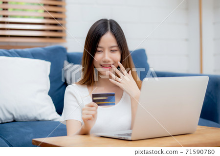 Young asian woman sit on sofa using laptop computer shopping online with credit card buy. 71590780