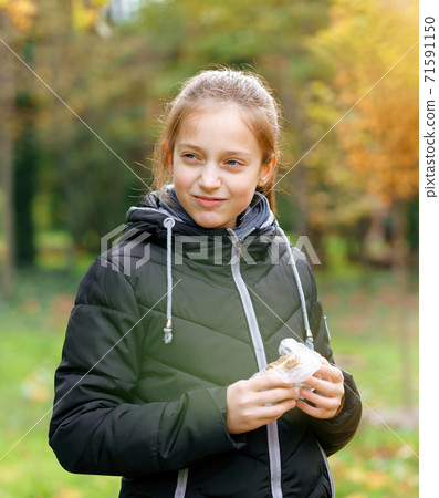 teen girl relaxing in autumn city park, walking and eating sandwich, beautiful nature 71591150
