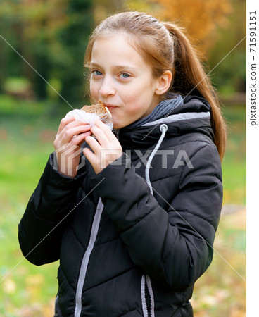 teen girl relaxing in autumn city park, walking and eating sandwich, beautiful nature 71591151