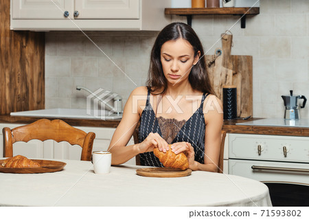 Mixed race woman eating fresh croissant in the kitchen in the morning Mixed race woman eating fresh croissant in the kitchen in the morning 71593802