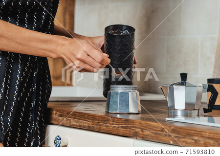 Close up view of hand pouring ground coffee into the geyser coffee maker Close up view of hand pouring ground coffee into the geyser coffee maker 71593810