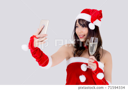 Beautiful portrait young asian woman in Santa holding glass of champagne and selfie with phone. Beautiful portrait young asian woman in Santa holding glass of champagne and selfie with phone. 71594334