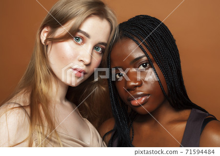 two pretty girls african and caucasian blond posing cheerful together on brown background, ethnicity diverse lifestyle people concept 71594484