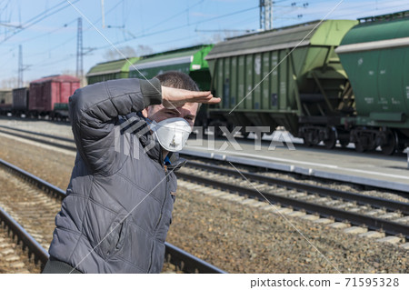 Man at the railway station waiting for his train, covering his face with his hand from the sun Man at the railway station waiting for his train, covering his face with his hand from the sun 71595328