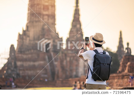 Happy tourist man with backpack Taking Photo by mobile smartphone, during visiting in Wat Chaiwatthanaram temple in Ayutthaya Historical Park, summer, solo, Asia and Thailand travel concept Happy tourist man with backpack Taking Photo by mobile smartphone, during visiting in Wat Chaiwatthanaram temple in Ayutthaya Historical Park, summer, solo, Asia and Thailand travel concept 71596475