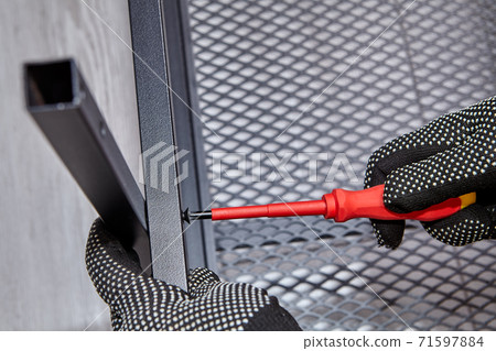 Worker is tightening bolts while mounting flat pack furniture with black steel frame. 71597884