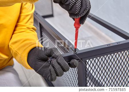 Assembler is tightening bolts while mounting flat pack furniture with black steel frame. 71597885