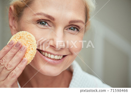 Smiling middle aged caucasian woman with facial sponge Smiling middle aged caucasian woman with facial sponge 71598466