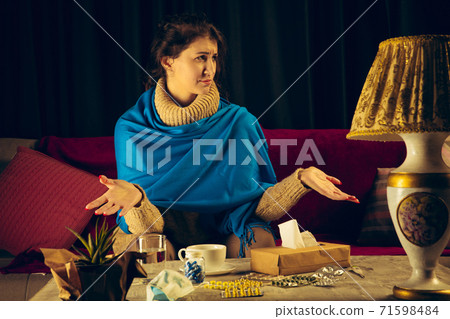 Woman wrapped in a plaid looks sick, ill, sneezing and coughing sitting at home indoors 71598484