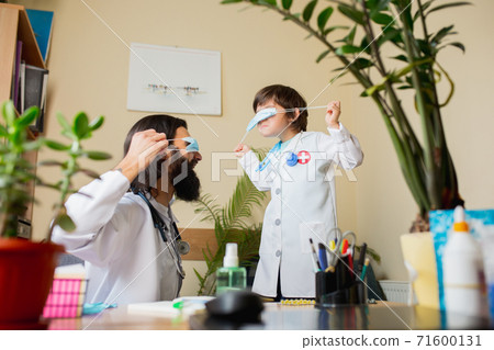 Paediatrician doctor examining a child while wearing face mask in comfortabe medical office Paediatrician doctor examining a child while wearing face mask in comfortabe medical office 71600131