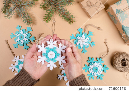 DIY instruction. Step by step tutorial. Making Xmas toy snowflake of felt. Step 7 - Tie threads on snowflakes in knots. Top view, flat lay. DIY instruction. Step by step tutorial. Making Xmas toy snowflake of felt. Step 7 - Tie threads on snowflakes in knots. Top view, flat lay. 71600158