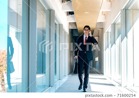 A young businessman in a suit calling on his smartphone in the office corridor 71600254