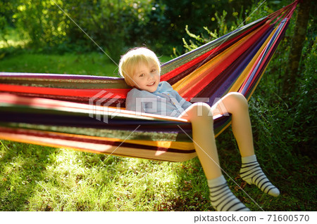 Cute little blond caucasian boy having fun with multicolored hammock in backyard Cute little blond caucasian boy having fun with multicolored hammock in backyard 71600570