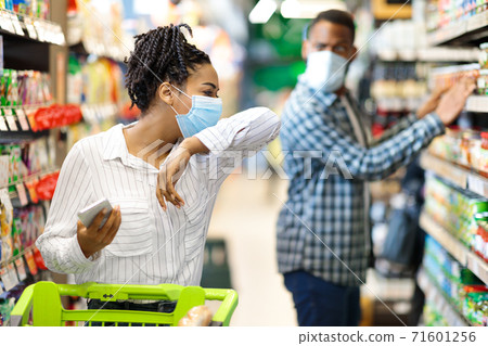 Sick African Woman Coughing In Elbow Wearing Mask In Supermarket Sick African Woman Coughing In Elbow Wearing Mask In Supermarket 71601256