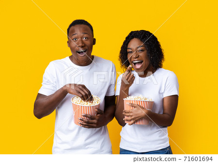 Laughing black man and woman eating popcorn on yellow background 71601694
