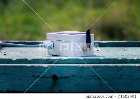 White transmitter with small solar panel and bees monitoring system on green wooden beehive, smart technology iot application White transmitter with small solar panel and bees monitoring system on green wooden beehive, smart technology iot application 71602401