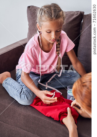 Girl helping her mother to sew Girl helping her mother to sew 71602630