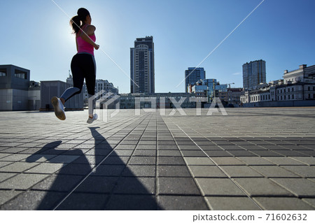 Rear view of fitness girl jogging on paved area 71602632