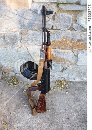 Kalashnikov AKM with high-capacity drum magazine near a stone wall 71603798