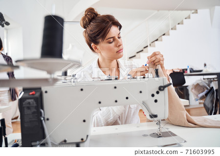 Woman seamstress sitting and sews 71603995