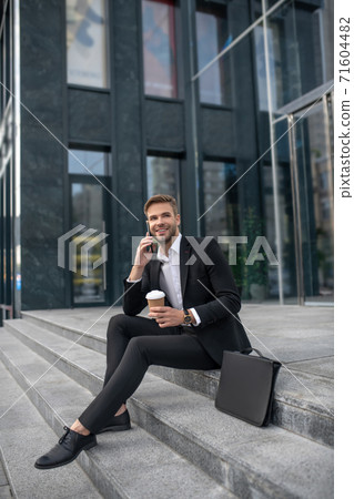 Elegant male businessman sitting on the steps and talking on the phone Elegant male businessman sitting on the steps and talking on the phone 71604482