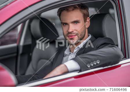 Young bearded male drivig red car, elbow out of window Young bearded male drivig red car, elbow out of window 71606496