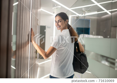 Dark-haired female with gym bag touching wooden wall, half-turned to camera 71610069