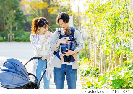 A couple walking outside while holding a baby A couple walking outside while holding a baby 71611075