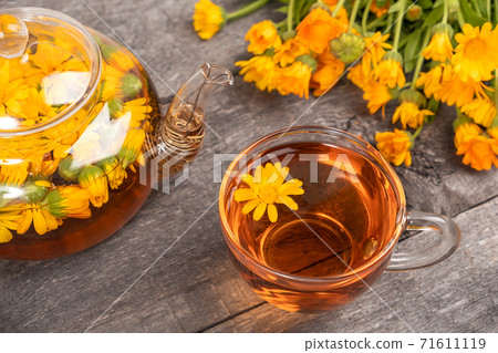 Cup of herbal tea and transparent teapot and marigold flowers on wood background. Calendula Tea Benefits Your Health concept Cup of herbal tea and transparent teapot and marigold flowers on wood background. Calendula Tea Benefits Your Health concept 71611119